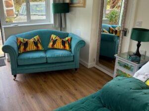 Teal two-seater sofa with abstract pillows and a teal chaise lounge in a bright living room.