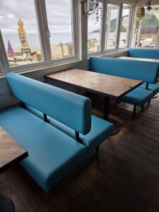 Custom blue upholstered booth seating with wooden tables facing a beachfront view
